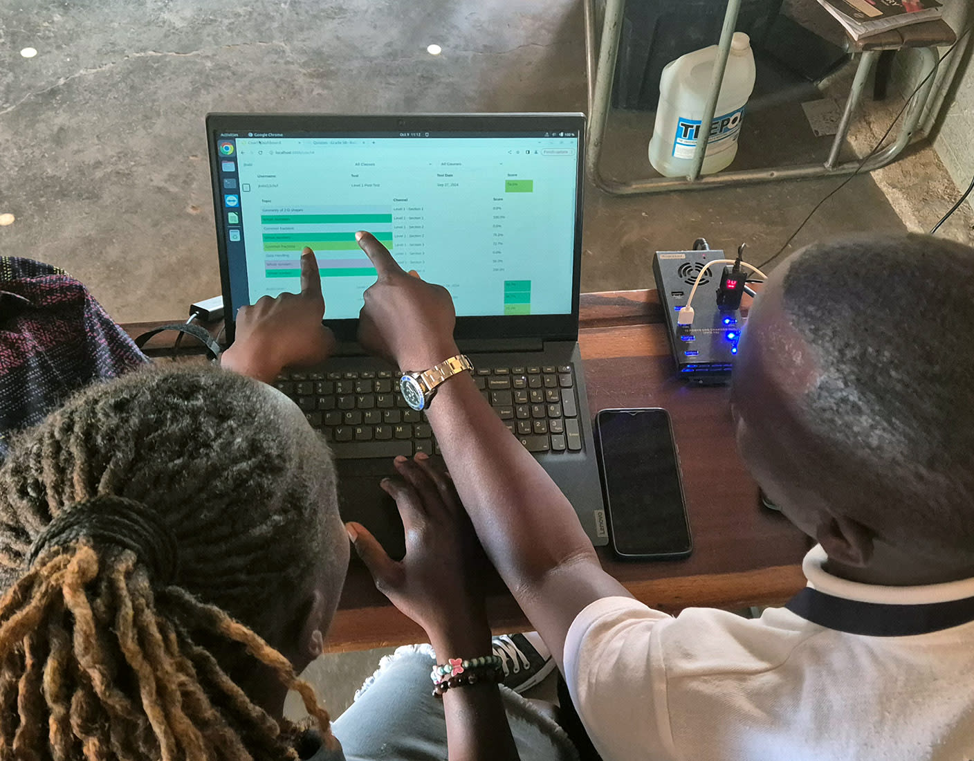 Two young individuals are intently working together on a laptop and both pointing to the chart displayed on the screen.
